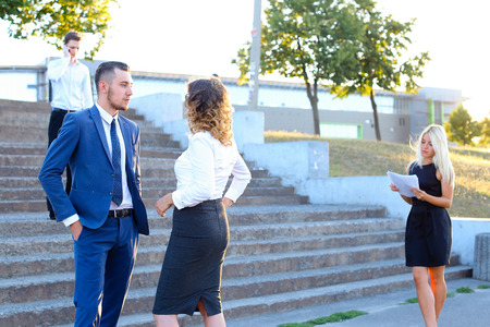 Lovely girl and handsome young guy talking on work items, solve important issues, discuss future annual report on background of trees, buildings and people outdoors. Man dressed in classic blue suit and white shirt with tie, girl with curly hair dressed iの写真素材