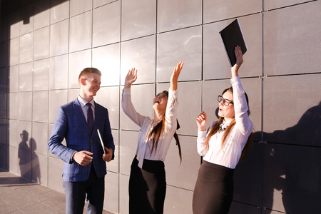 Modern handsome male man and two pretty confident girl, successful young office workers, businessmen, students communicate, laugh, rejoice successfully concluded transaction, end working day, talk on various topics, discuss working moments, holding in hanの写真素材