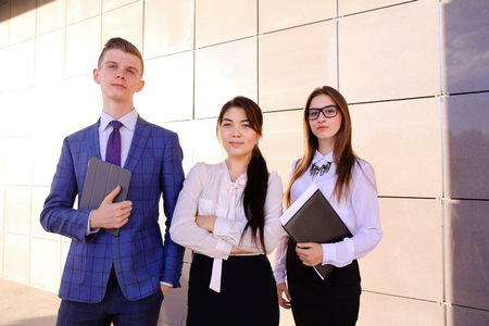 Modern handsome male man and two pretty confident girl, successful young office workers, businessmen, students holding in hands documents, smiling and posing to photographer camera, taking pictures for company brochures, advertising office clothes and staの写真素材