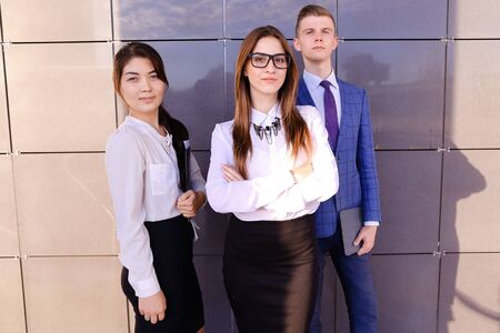 Modern handsome male man and two pretty confident girl, successful young office workers, businessmen, students holding in hands documents, smiling and posing to photographer camera, taking pictures for company brochures, advertising office clothes and staの写真素材