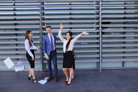 Three young adult attractive people, two women and one men students, prospective entrepreneurs  scatter paper and rejoice success, implementation of annual of business plan, end of working day, beginning of weekend, smiling and laughing and standing of buの写真素材