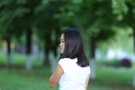 Girl female teenager with black hair in a bob white east Asian woman green park with a backpack background. Lady holds, dials, push your finger, smiling, looking into the camera, talking on the phone happy portrait.の写真素材