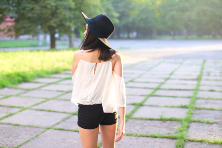 female hat nature summer sun sunset looks pleased. azitka woman black hair white shirt black shorts dancing around the trees looking at the camera. portrait.の写真素材