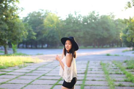 female nature keeps his hat summer sun sunset looks pleased. azitka woman black hair white shirt black shorts dancing around the trees looking at the camera. portrait. spinningの写真素材
