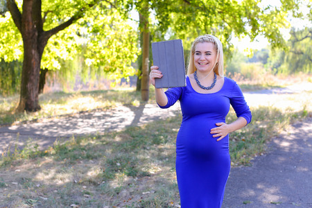 Gorgeous Contemporary Young Feminine Carries Baby Under Heart. Girl Chatters With Husband About Well-Being or Informs Parents About Anticipated Date of Childbirth. Female With Blond Braided Plait Hair in Front Dressed in Long Blue Dress With Sleeves, Arouの写真素材