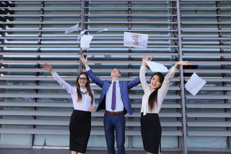 Three young adult attractive people, two women and one men students, prospective entrepreneurs  scatter paper and rejoice success, implementation of annual of business plan, end of working day, beginning of weekend, smiling and laughing and standing of buの写真素材