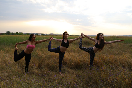 Female performing warm-up exercises and stretching, focus on correct posture execution, photographed for advertising of catalog womens sportswear or sports complex in wide field outdoors. Girl with shoulder-length hair dressed in pink top and black legginの写真素材