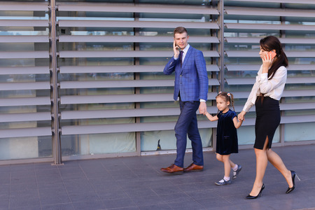 Successful young handsome male man young father and modern girl, young mother hold gadgets  in hand, mobile phones and talking on them, solve operational issues, agree to meet, negotiate with business partners, reviewing documents in hurry to work and keeの写真素材