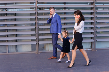 Successful young handsome male man young father and modern girl, young mother hold gadgets  in hand, mobile phones and talking on them, solve operational issues, agree to meet, negotiate with business partners, reviewing documents in hurry to work and keeの写真素材