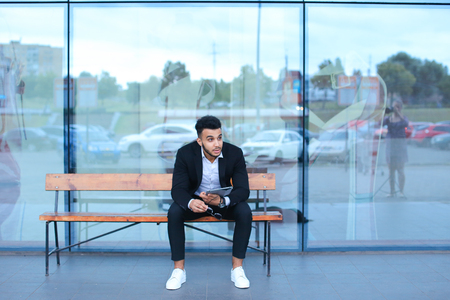 Entrepreneur smiling man  puts on sunglasses uses tablet and looks at. Young handsome businessman arab muslims in business center wearing dressed in black elegant suit on building background.の写真素材