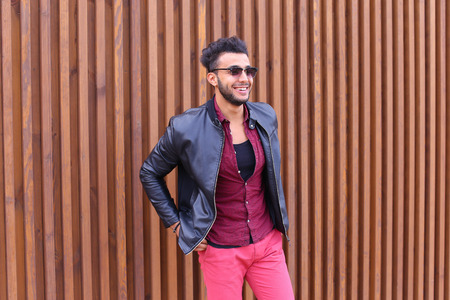 Attractive Young Adult Arabian Man Poses Into Camera, Corrects Hairstyle and Smiles, Waits For Meeting and Advertises Male Sunglasses, Looks Around Wearing Glasses and Stands on Background of Wooden Panel Stairs Outdoors. Stylish Male With Dark Hair Dressの写真素材