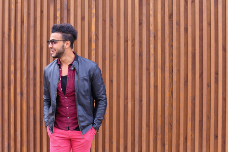 Attractive Young Adult Arabian Man Poses Into Camera, Corrects Hairstyle and Smiles, Waits For Meeting and Advertises Male Sunglasses, Looks Around Wearing Glasses and Stands on Background of Wooden Panel Stairs Outdoors. Stylish Male With Dark Hair Dressの写真素材