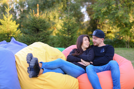 Pair of lovers of young attractive people sitting in soft yellow and red chair.  Young people cute communicate, plan to travel, choosing interior of apartment, guy tells about one of following general recreation, boyfriend and girlfriend smiling, hugging の写真素材