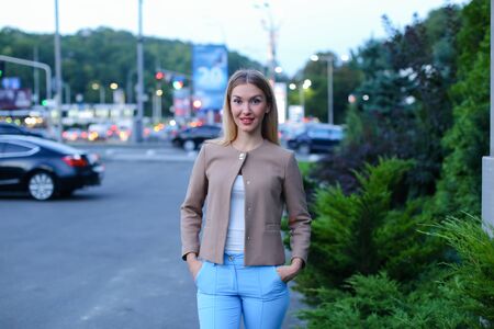 Women with blond hair european appearance smiles and removed advertising for clothes and accessories, womens magazine or waiting for friend. Girl dressed in bright light blouse, beige jacket and blue trousers. Concept of stylish girl, shooting advertisingの写真素材