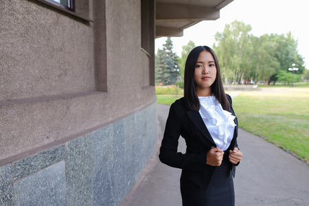 Ambitious modern young women woman, business woman, student posing for camera, smiling, change posture standing on background of  business center outdoors.Woman with black hair, dressed in white blouse and classic jacket. Concept of business, advertising の写真素材