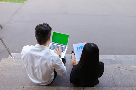 Young contemporary confident perspective entrepreneurs, students chatting with each other, using laptops, drawing up business plan, discuss working moments, share of business ideas, solve problems and reads important documents sitting on stair of businessの写真素材
