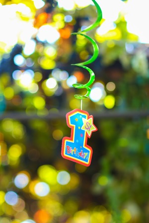 Fragment decor, childrens holiday decorations, thematic birthday, photography festive figures, first year of life, blue and orange hanging on green spiral on background of foliage in courtyard outdoors. Concept birthday, childrens party, decor, theme partの写真素材