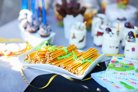 In photo depicts variety of goodies, delicious food, clear jars with cottage cheese soufflÃ© with layer of pastry topped with fruit and straws, chocolate long candy skewers in patterned white small vase, chocolate balls in coconut flakes with blue straw, の写真素材