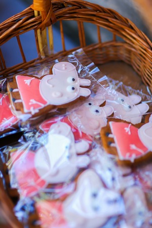 On photo depicts pink gingerbread with pattern Peppa pig, cartoon character, which sealed in transparent cellophane and stacked in brown wicker basket, which is located near other treats on table outdoors. Concept birthday, childrens holiday, holiday tablの写真素材