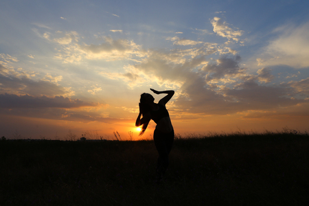 Female with beautiful figure takes yoga postures, gymnastics and ballet spends stretching and meditating, posing for advertising shoot fitness studio, healthy energy drink, dancing belly dancing among wide field on background of yellow sunset and beautifuの写真素材