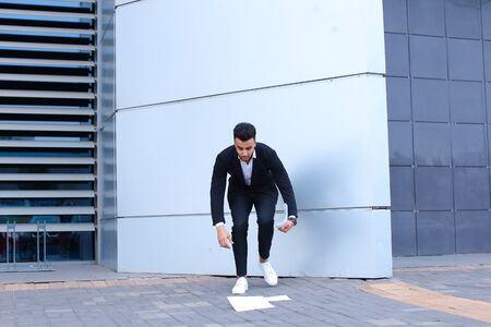 Arabic businessman handsome masculine guy drops and collects important papers or documents.Bearded man dressed in classic suit, black pants, jacket , white shirt and sneakers,  on hand is watch. Concept of securities, Business Meeting, busy Dealer.の写真素材