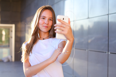Beautiful cheerful young female student girl holding white phone, smilingの写真素材