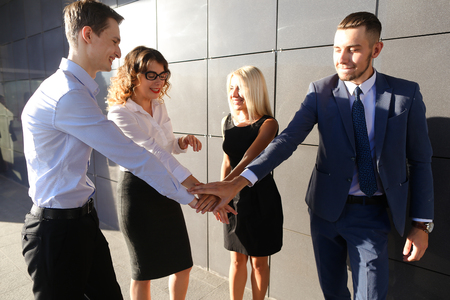 Four young adult active people, two women and two men students, prospective entrepreneurs rejoice success, raise hands up, implementation of annual of business plan, the end of working day, beginning of weekend, smiling and laughing and standing of busineの写真素材