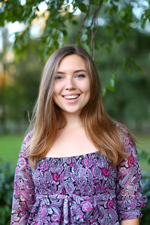 Nice girl of European appearance changing hand position and posture, photographed for shooting of advertising, happy smiling female beautiful wide smile and enjoying life, breathing  fresh air in green park among trees on hot summer day. Girl of European の写真素材