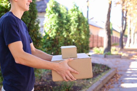 Deliveryman Carring Parcel and Giving it and Smiling. International Staffing Company Shows That Courier of Company Always Ready to Work at Any Time and Any Day, Young Man of European Appearance in Uniform, With Broad Smile and Good Mood on Background of Hの写真素材