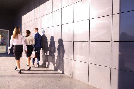 Successful male guy, businessman and two pretty young women, business people, students go in opposite direction from camera and discuss working day, returning from lunch break, study plans and kept paper in hands, graphics, and view them and go along of gの写真素材