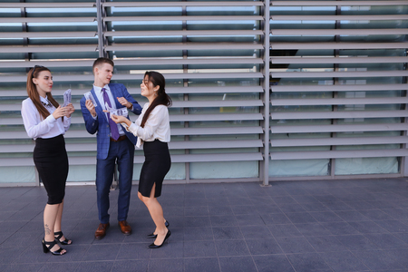 Two beautiful successful young women, business woman and confident young guy male entrepreneur, held personality, hold in hands money, dollar and scattered, communicate with each other, posing and smiling to camera, laugh, dance and enjoy life, stand agaiの写真素材