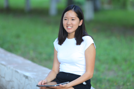 Girl female teenager with black hair in a bob white east Asian woman green park background. Lady holding plate and presses a finger, smiling, looking into the camera.の写真素材