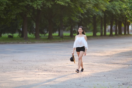 female nature keeps his hat summer sun sunset looks pleased. azitka woman black hair white shirt black shorts out trees around.の写真素材