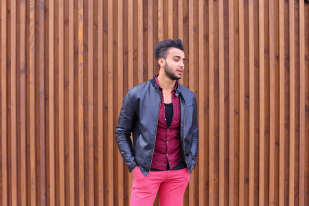 Charismatic Young Businessman Muslim Man Comes Closer to Camera, Smiles and Poses For Camera on Photographer, Shows Gestures, Laughs, Advertises Clothing on Wooden Panel Background Stairs Outdoors. Stylish Young Man With Dark Hair and Sunglasses Dressed iの写真素材