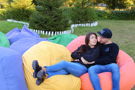Pair of lovers of young attractive people sitting in soft yellow and red chair.  Young people cute communicate, plan to travel, choosing interior of apartment, guy tells about one of following general recreation, boyfriend and girlfriend smiling, hugging の写真素材