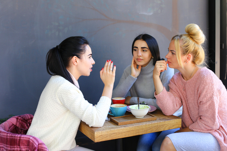 Concept female friendship, meeting, lunch. Three beautiful women sitting incafe smiling, talking, telling secrets, drink coffeeの写真素材