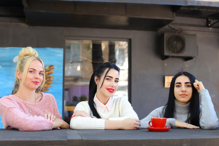 Concept female friendship, meeting, lunch. Three beautiful women sitting incafe smiling, talking, telling secrets, drink coffeeの写真素材