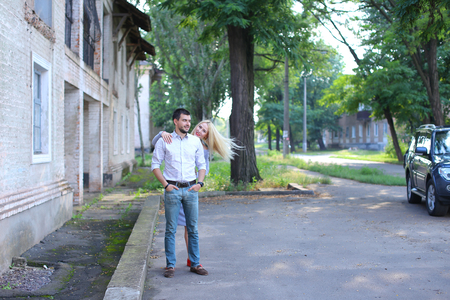 Girlfriend and boyfriend standing next to each other, posing, talking and laughing, hugging on street. Girl dressed in midi gray dress and red slip-on, guy straight, keeping hands in pants pockets and looking directly into camera, he dressed in blue jeansの写真素材