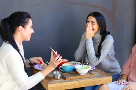 Concept female friendship, meeting, lunch. Three beautiful women sitting incafe smiling, talking, telling secrets, drink coffeeの写真素材