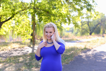 Dazzling Contemporary Young Adult Feminine of European Appearance Carries Baby Under Heart. Girl Leisurely Walking and Chatters on Phone With Husband About Well-Being and Appoint Meeting at Cinema or Says Family Doctor About State of Health. Female With Bの写真素材
