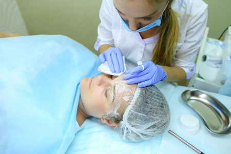 Blonde girl European appearance, professional engaged in reconstruction of eyebrows responsibly preparing to start work mikrobleyding eyebrows, eyebrows customer focused prepares women to paint application, choose appropriate shade for tattoo, next to couの写真素材