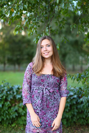 Nice girl of European appearance changing hand position and posture, photographed for shooting of advertising, happy smiling female beautiful wide smile and enjoying life, breathing  fresh air in green park among trees on hot summer day. Girl of European の写真素材