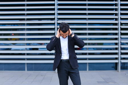 Entrepreneur shows neck pain tired looking  at the camera. Young handsome businessman arab muslims in business center wearing dressed in black elegant suit on building background.の写真素材