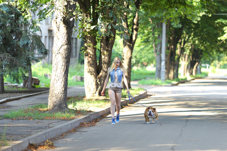 Young beautiful woman girl lady blond hair with red lips in casual style american bulldog. Woman plays with dog glad, laughing, happy and inspired walking goes.の写真素材