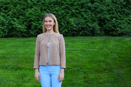 Women with blond hair european appearance smiles and removed advertising for clothes and accessories, womens magazine or waiting for friend. Girl dressed in bright light blouse, beige jacket and blue trousers. Concept of stylish girl, shooting advertisingの写真素材