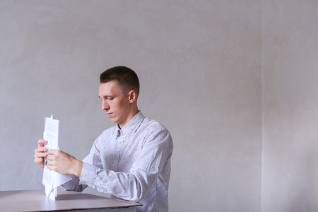 Entrepreneur adds documentation and completes work day. Men with short hair and blond hair sitting on chair at white table in office and dressed in white classic shirt. Concept of businessman office work, sedentary routine work documentation, successful yの写真素材