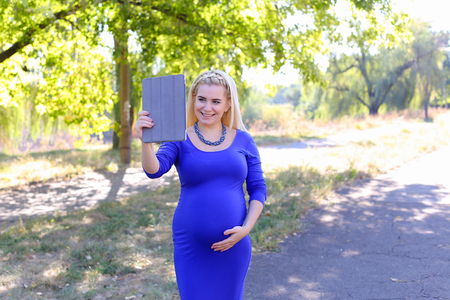 Gorgeous Contemporary Young Feminine Carries Baby Under Heart. Girl Chatters on With Husband About Well-Being or Informs Parents About Anticipated Date of Childbirth. Female With Blond Braided Plait Hair in Front Dressed in Long Blue Dress With Sleeves, Aの写真素材