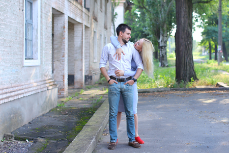 Girlfriend and boyfriend standing next to each other, posing, talking and laughing, hugging on street. Girl dressed in midi gray dress and red slip-on, guy straight, keeping hands in pants pockets and looking directly into camera, he dressed in blue jeansの写真素材