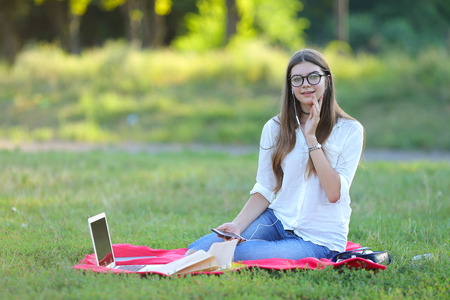 girl listening to music on the nature of the glasses. in the park for a laptop unravels headphones and holding a mobile phoneの写真素材