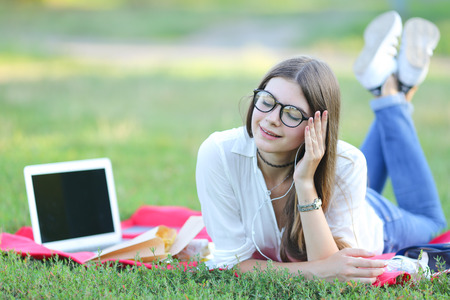 beautiful girl lies with the outdoors with a laptop. student in glasses with headphones running and smilingの写真素材